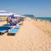 Lettini e ombrelloni blu disposti lungo la spiaggia, pochi bagnanti in acqua.