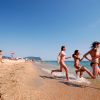 Ragazzi corrono verso il mare lungo una spiaggia sabbiosa.