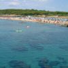 Spiaggia affollata con persone in acqua, canoa e ombrelloni sulla sabbia.