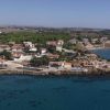 Veduta aerea di una penisola con costruzioni costiere, circondata da un mare blu intenso.