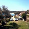 Vista di una strada con auto parcheggiate, alberi e vista sul mare in lontananza.