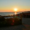 Sole al tramonto che illumina un ristorante vicino al mare, con cielo arancione.