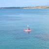 Persona su un kayak rosso in mare aperto con sfondo di costa distante.
