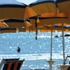 Ombrelloni gialli e blu sulla spiaggia, con persona che nuota nel mare sullo sfondo.
