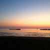 Un tramonto sul mare con cielo sfumato di arancione e blu, piccole onde e scogli in lontananza.