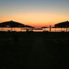 Spiaggia al tramonto con ombrelloni silhouette e cielo colorato.