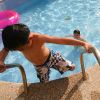 Due bambini in piscina. Uno esce usando la scaletta, l'altro nuota vicino a un salvagente rosa.
