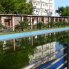 Piscina lunga con acqua scura, vegetazione e un edificio bianco sullo sfondo.