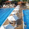 Piscina all'aperto con ombrelloni bianchi e persone che nuotano.