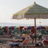 Spiaggia sabbiosa con ombrelloni colorati e lettini occupati.
