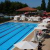 Piscina all'aperto con corsie e lettini sotto ombrelloni bianchi.