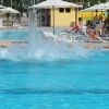 Schizzi d'acqua in una piscina, circondata da ombrelloni e lettini.