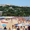 Spiaggia affollata con ombrelloni colorati, mare e collina sullo sfondo.