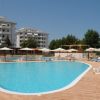 Una piscina con lettini e ombrelloni bianchi, circondata da edifici e alberi.