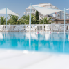 Piscina circondata da lettini bianchi e ombrelloni bianchi, con palme e edifici sullo sfondo.