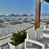 Terrazza con sedie bianche, vista su una spiaggia con ombrelloni grigi.