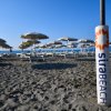 Ombrelloni e lettini su una spiaggia sabbiosa con il mare sullo sfondo.