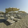 File di sdraio e ombrelloni bianchi su una spiaggia sabbiosa sotto un cielo limpido.