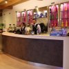 Due baristi dietro un banco moderno con scaffali di bottiglie. Due persone fanno un ordine.