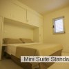Una mini suite con letto matrimoniale, mobili chiari e piccola finestra.