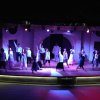 Gruppo di persone balla su un palco illuminato con luci colorate.