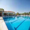 Una piscina con lettini e ombrelloni blu sotto un cielo limpido, circondata da palme.