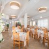 Interno di un ristorante con tavoli apparecchiati, sedie in legno chiaro e fiori bianchi.