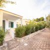 Bungalow giallo con veranda, circondato da vegetazione e sentiero pavimentato.