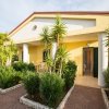 Casa gialla con veranda, circondata da palme e giardino curato.