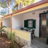 Un bungalow giallo con veranda, tavolo e sedie sotto alberi.