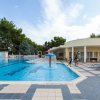 Una piscina con una fontana a fungo, alberi e lettini intorno.