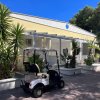 Edificio giallo con un veicolo da golf parcheggiato davanti, circondato da piante.