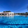 Grande piscina blu all'aperto con persone che nuotano e un edificio bianco sullo sfondo.