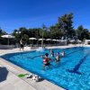 Persone fanno acquagym in piscina all'aperto, circondate da ombrelloni e piante.