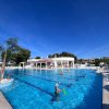 Piscina all'aperto con bagnanti e un edificio bianco sullo sfondo, cielo blu sopra.