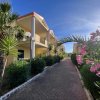 Viale alberato con edifici a due piani, palme e fiori rosa, sotto un cielo blu luminoso.