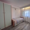 Una camera con letto singolo, armadio, tende bianche e parquet grigio.
