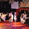 Ballerini in abiti bianchi si esibiscono su un palco illuminato.