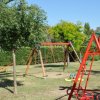 Area giochi con altalene rosse e alberi verdi.