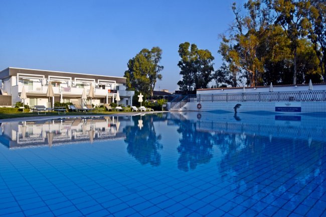 Piscina grande con villette e alberi sullo sfondo.