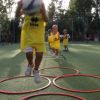 Bambini in tuta gialla saltano tra cerchi rossi su un campo da gioco.