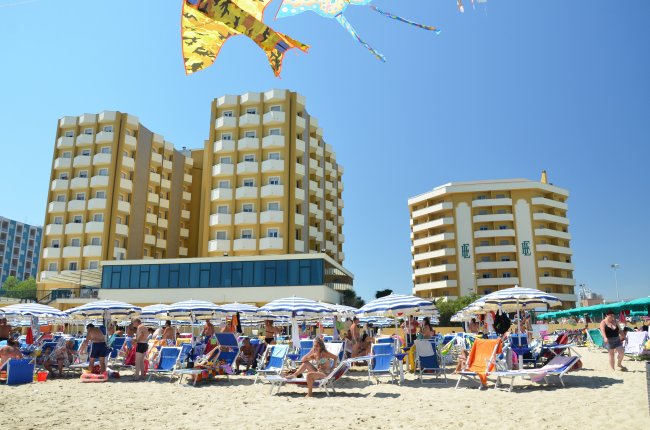 Spiaggia affollata, edifici alti sullo sfondo.