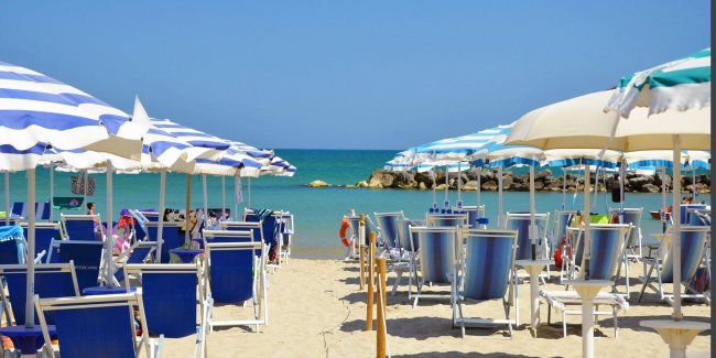 Ombrelloni e lettini blu su spiaggia sabbiosa.