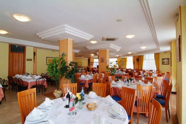 Sala ristorante con tavoli apparecchiati e sedie in legno.