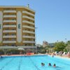 Piscina con persone che nuotano e un edificio giallo con balconi.