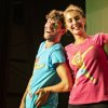 Due persone sorridenti con magliette colorate su un palco.