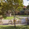 Giardino con tavoli e sedie in legno, al centro una fontana e alberi intorno.