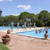 Piscina all'aperto con bambini e istruttori in blu, alberi sullo sfondo.