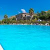 Grande piscina all'aperto con sdraio, palme e cielo blu.