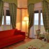 Salotto con divano rosso, tavolino e sedie, tende verdi e balcone vista mare.